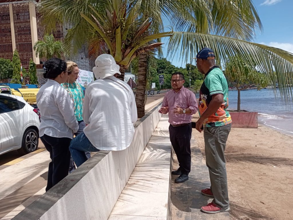 Participants from Papua in discussion with the mentors under a palm tree at a beach area. 
