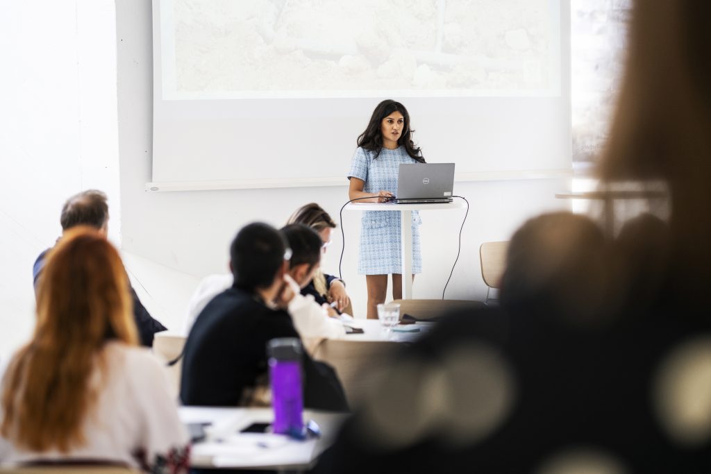 A woman standing in front of a power point presentation talking to an audience. 