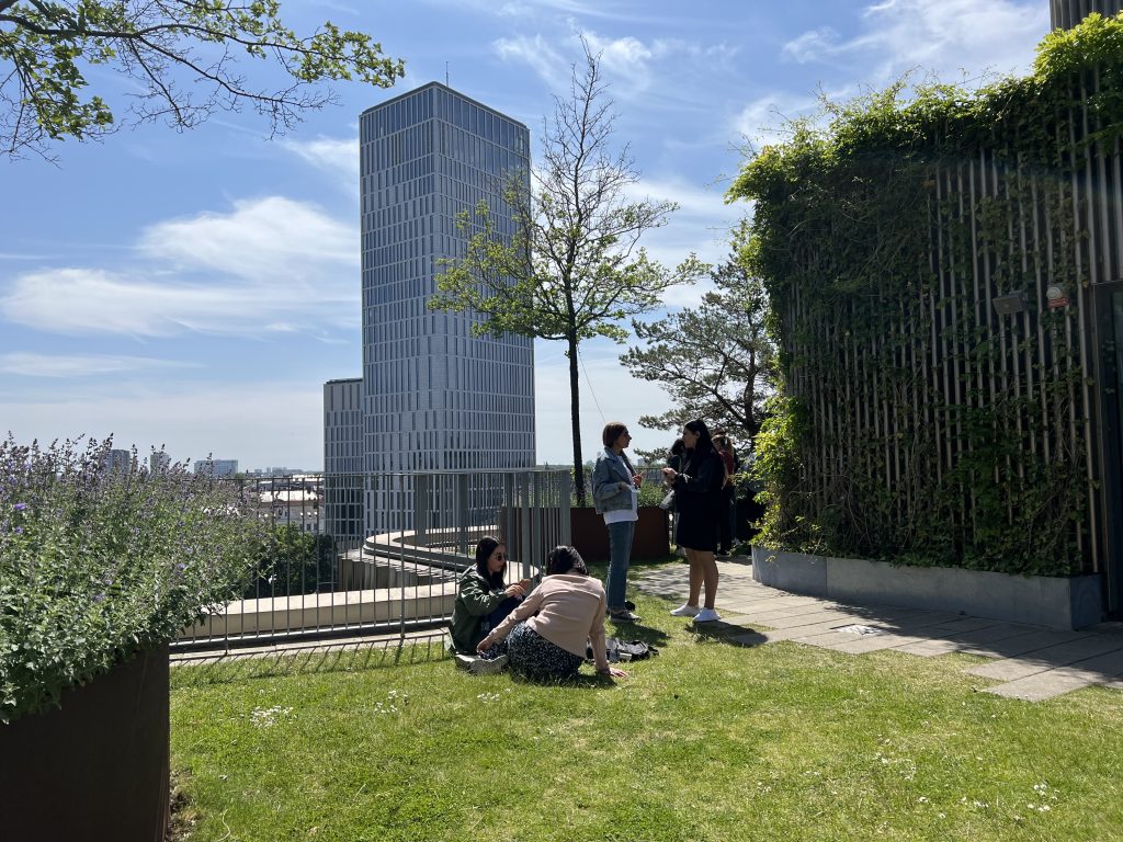 People sitting and standing on a green roof with a vue in front of them of a tall building. 